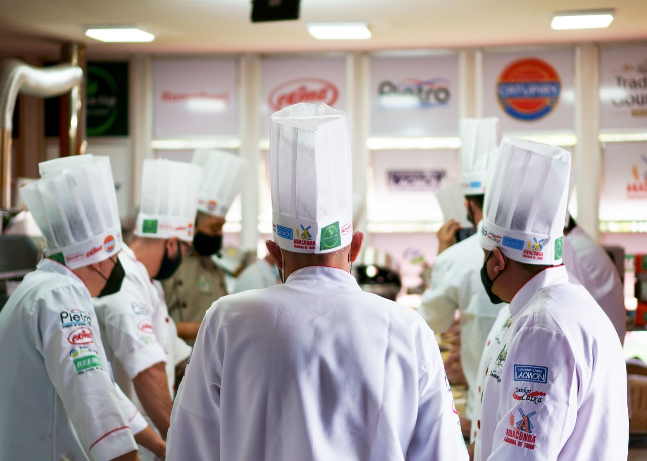A group of professional chefs in white uniforms and hats working together in a busy commercial kitchen.