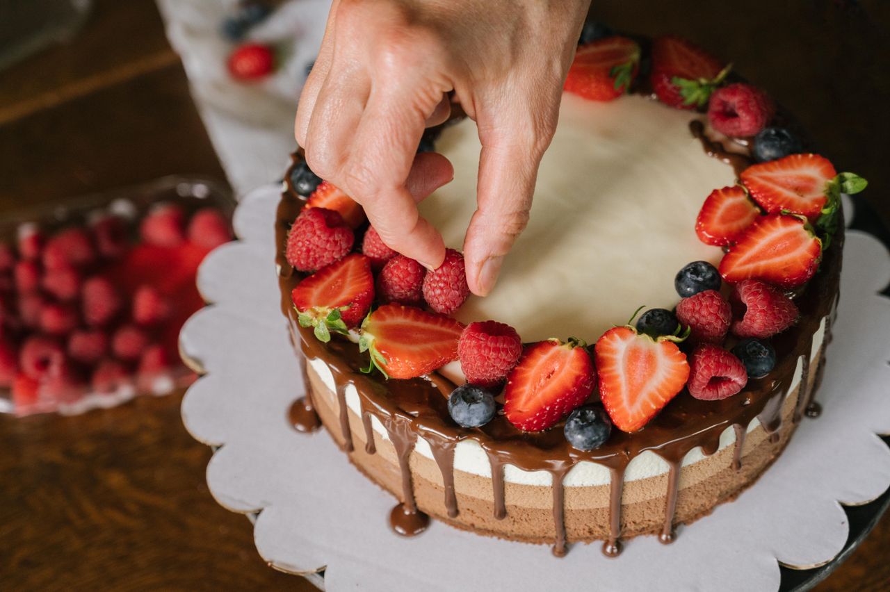 Home Hand placing fresh berries on a chocolate-covered cake, creating a delicious dessert.